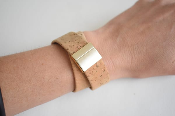 Recyled Jewellery: A close-up of a person's wrist wearing a stylish watch with a beige recycled cork strap and a shiny gold clasp on a white background. @ Reblack Shop