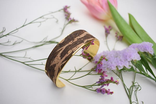 Recyled Jewellery: A wooden bangle, crafted from recycled jewellery, with a natural pattern sits on a white surface, surrounded by delicate pink tulip and purple and pink wildflowers. @ Reblack Shop