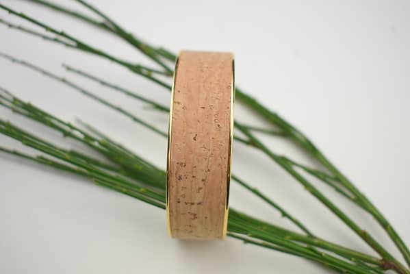 Recyled Jewellery: A cylindrical cork object, adorned with recycled jewellery, stands on a white background, surrounded by slender green grass blades spreading outward. @ Reblack Shop