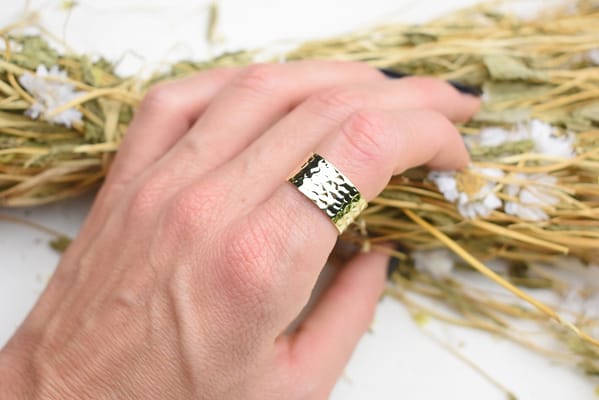 Recyled Jewellery: A close-up of a hand wearing a recycled decorative ring on the ring finger, resting on a bed of dried flowers and grass. @ Reblack Shop