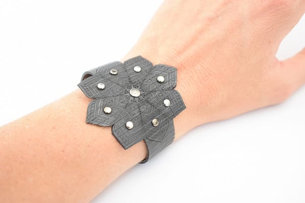 Recyled Jewellery: A person wearing a unique, eco-friendly dark gray floral-shaped bracelet with silver stud accents, displayed on their wrist against a white background. @ Reblack Shop