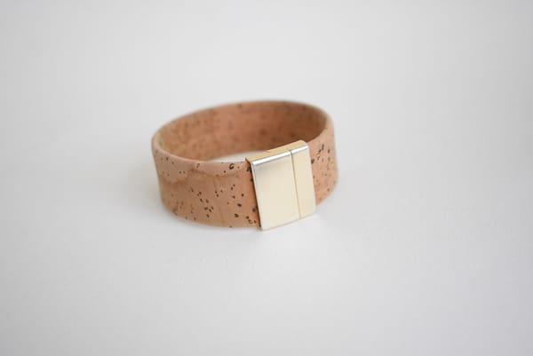 Recyled Jewellery: A recycled cork bracelet with a smooth, light tan surface featuring dark speckles, finished with a square, metallic gold-tone clasp, displayed against a plain white background. @ Reblack Shop