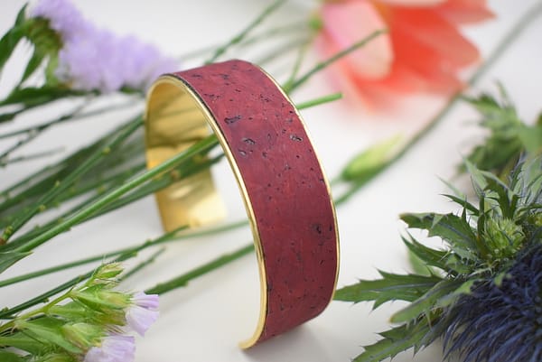 Recyled Jewellery: A close-up image of a red and gold recycled jewellery bracelet surrounded by colorful flowers, highlighting its elegant texture and vibrant color contrast. @ Reblack Shop