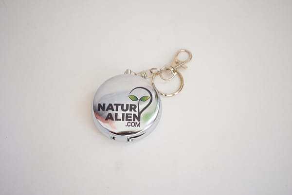 Recyled Jewellery: A small, eco-friendly metallic keychain featuring a logo with the text "naturalien.com", designed with an alien graphic. The keychain has a circular shape and includes a chain with a clasp @ Reblack Shop