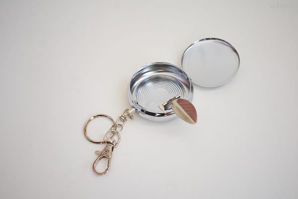 Recyled Jewellery: A small, portable keychain mirror, repurposed from eco-friendly jewelry materials, lying open with one mirror facing up and the other at an angle, set against a plain light background. @ Reblack Shop