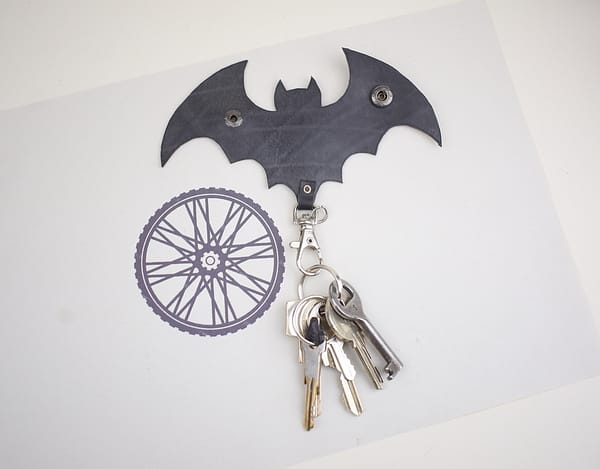 Recyled Jewellery: A bat-shaped key holder mounted on a wall with a recycled jewellery design beside it. A set of keys hangs from the holder. @ Reblack Shop