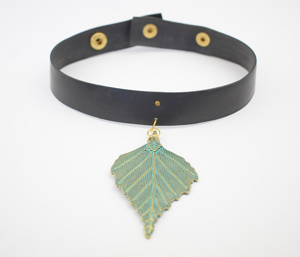 Recyled Jewellery: A black choker necklace featuring an eco-friendly gold and turquoise pendant shaped like a leaf, laid out on a white background. @ Reblack Shop