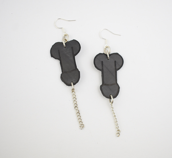 Recyled Jewellery: A pair of Penis Earrings shaped like bones, crafted from black material with a matte finish, each hanging from a silver chain and hook, against a plain white background. @ Reblack Shop