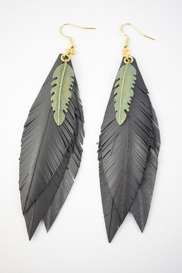Recyled Jewellery: A pair of Feather Cut and Patina earrings, crafted from repurposed jewelry materials with one colored in matte black and the other in a metallic gold accent, dangling from golden hooks against a white background. @ Reblack Shop
