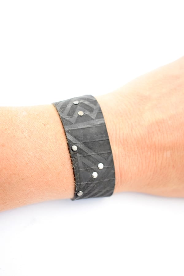 Recyled Jewellery: A close-up of a wrist wearing a Maori Tribal Bracelet with a geometric pattern and small silver studs, against a white background. @ Reblack Shop