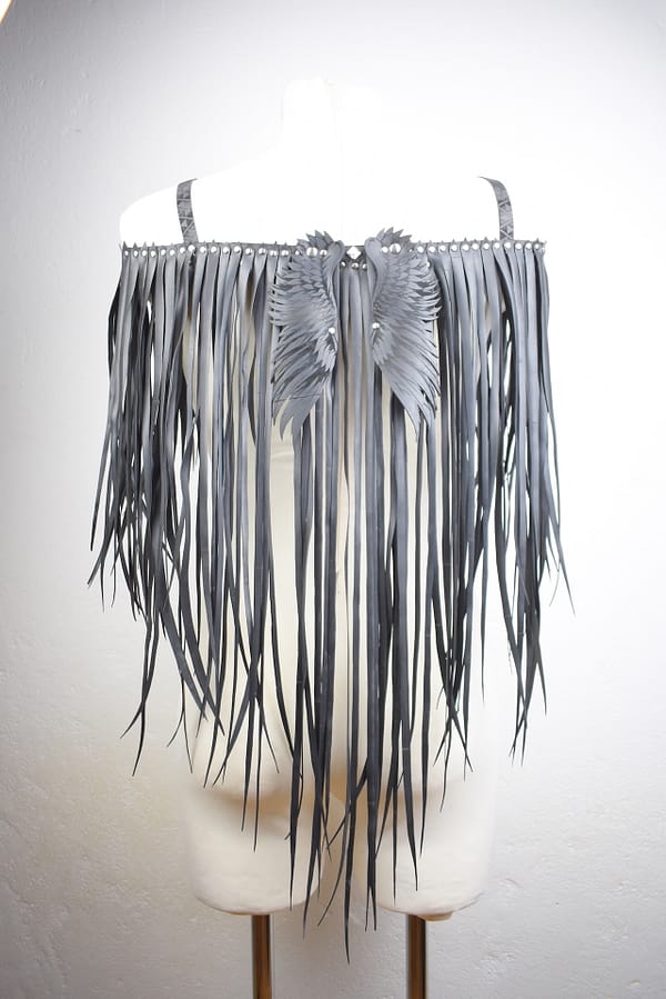 Recyled Jewellery: A Fallen Angel leather fringe harness displayed on a mannequin, featuring detailed angel wings repurposed from jewelry on the shoulders, set against a white textured wall. @ Reblack Shop