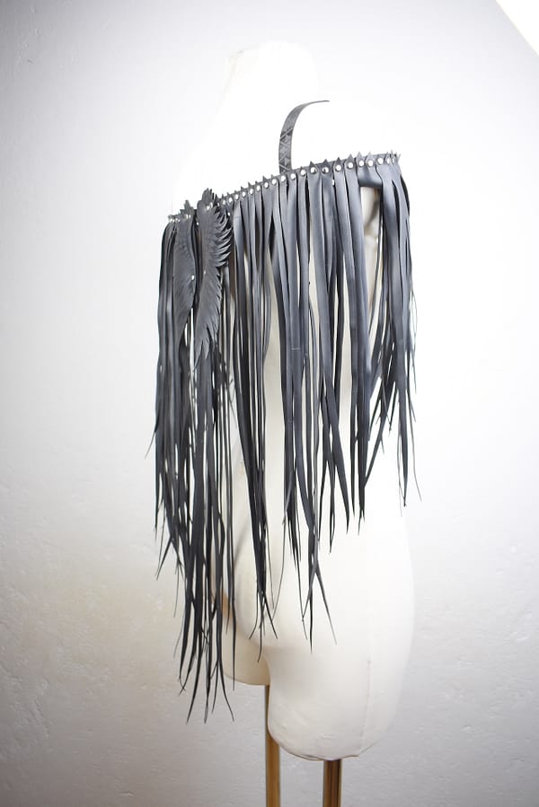 Recyled Jewellery: A white mannequin displaying a Fallen Angel leather shoulder accessory with long fringes and embellished with repurposing jewelry metal studs, against a neutral background. @ Reblack Shop